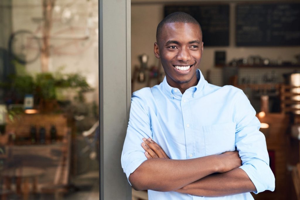 Black entrepreneur leaning on the door to his shop, representing local business competing with big box retail