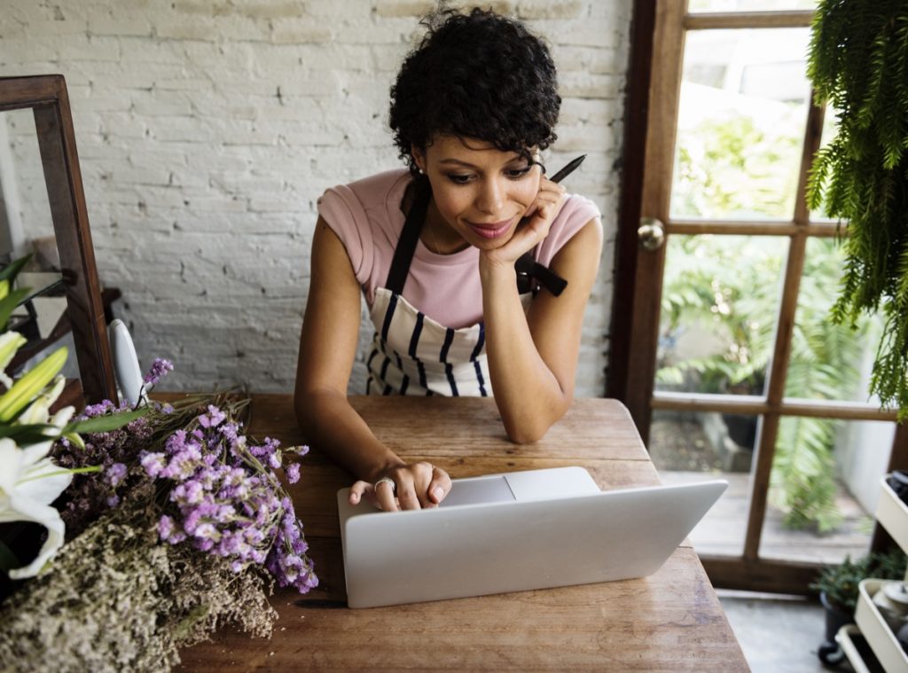 Woman Using Laptop at a Flower Shop, representing local business competing with big box retail