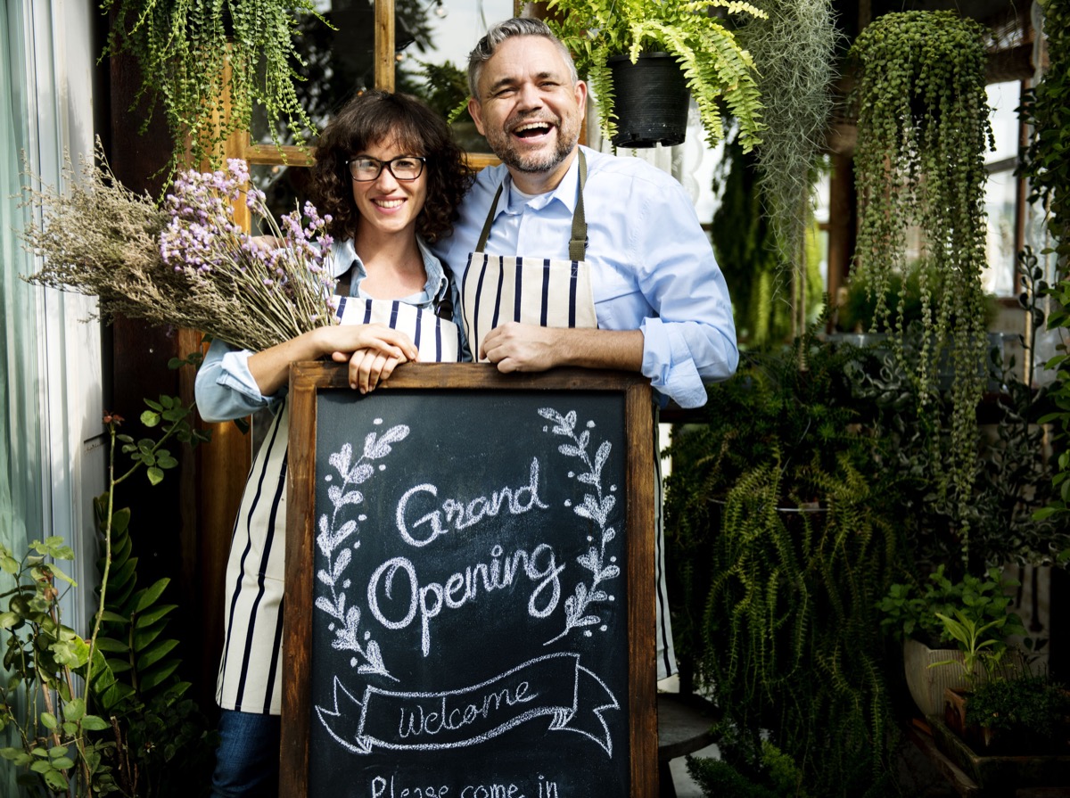 Adult Man and Woman Standing with Grand Opening Sign; new location concept